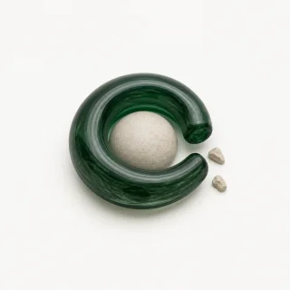 An open green glass loop losing small stone fragments